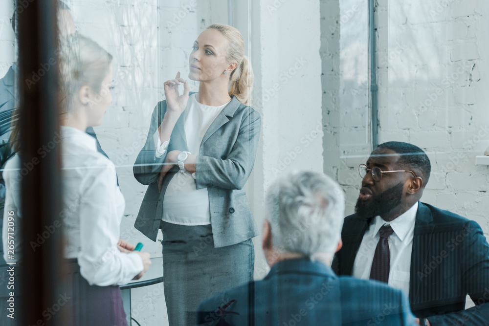 Wall mural pregnant businesswoman standing and pointing with finger near multicultural coworkers