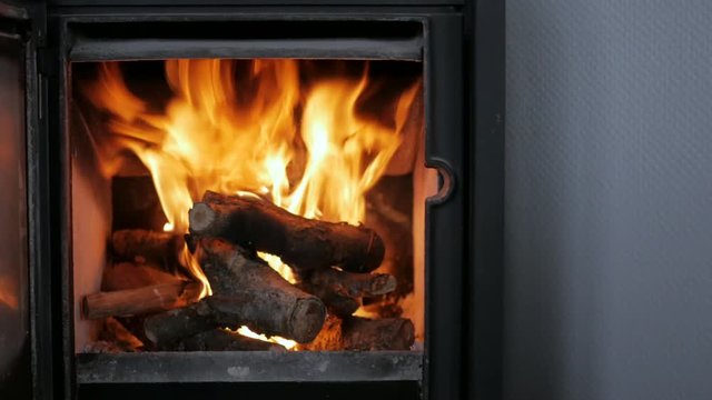 Close up of wood burning stove with open door and fire tools in living room newly lit and burning lively with big red and orange flames. Sliding shot from left to right.