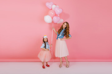 Family portrait of attractive young mother and little daughter posing on pink background with...