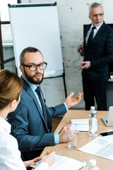 handsome bearded man talking with businesswoman while gesturing near business coach