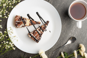 On the plate, two slices of cheesecake with tea and flowers, for congratulations on a dark background