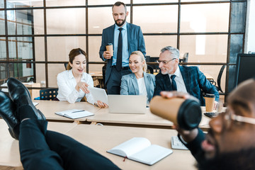 selective focus of cheerful businessmen and businesswomen looking at digital tablet near african american coworker