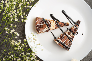 On the plate, two slices of cheesecake with tea and flowers, for congratulations on a dark background