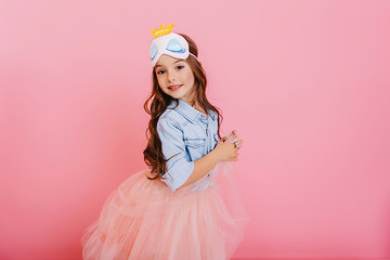 Cute beautiful carnival kid having fun isolated on pink background. Pretty little girl with long brunette hair, in tulle skirt, princess mask expressing happiness to camera, celebrating children party © Look!