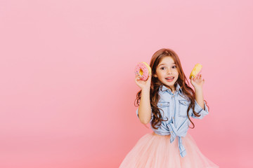 Obraz na płótnie Canvas Excited joyful young pretty girl in tulle skirt expressing positivity, having fun to camera isolated on pink background. Happy childhood with tasty dessert. Place fot text
