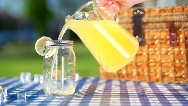Lemonade being poured from a glass pitcher into a mason jar.