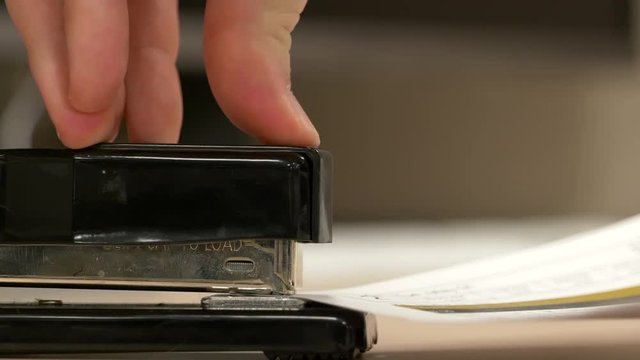 A close up from the side of a black stapler stapling pieces of paper together in slow motion.