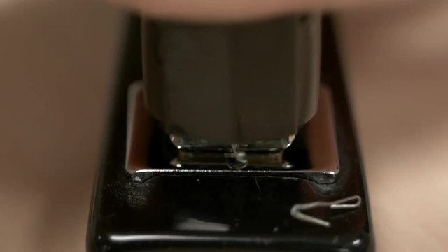 A hand hitting a black stapler with no paper in it a bunch of times knocking staples out.