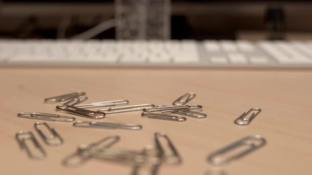 A hand full of paper clips slowly dropping onto an office desk a little bit at a time.