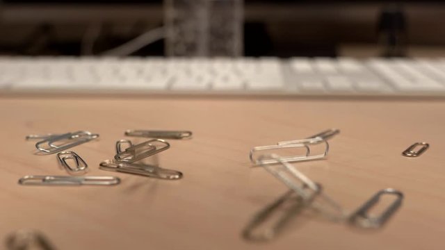 A hand full of paper clips slowly dropping onto an office desk in slow motion a little bit at a time.