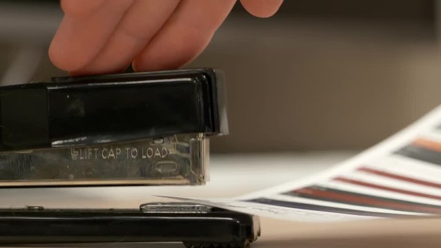 A close up from the side of a black stapler stapling pieces of paper together in slow motion.