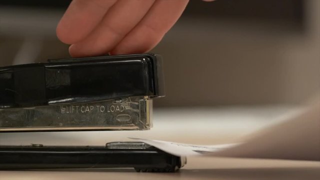 Side view of a black stapler stapling some paper together in really slow motion.