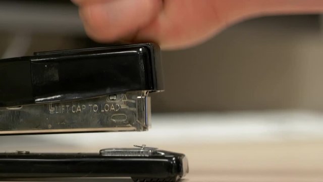A profile view hand hitting a black stapler with no paper in it a bunch of times knocking staples out. In slow motion.
