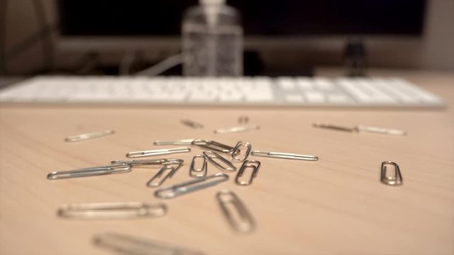A hand full of paper clips slowly dropping onto an office desk in super slow motion all at once.