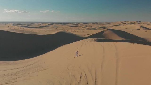 Aerial of desert sand dunes with motocross riders and a ​man running.