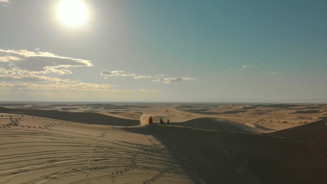 Aerial of desert sand dunes with motocross riders and a ​man running.