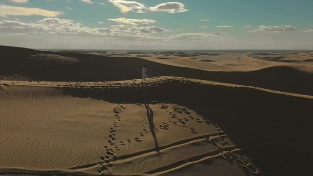Aerial of desert sand dunes with motocross riders and a ​man running.