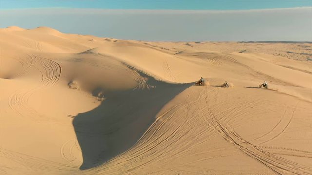 Aerial of desert sand dunes with motocross riders and a ​man running.