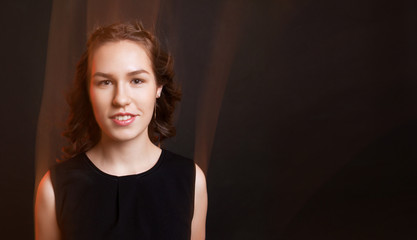 Portrait of young girl with flying hair. Cute teen girl smiling. Mixed light. Black background, black dress.