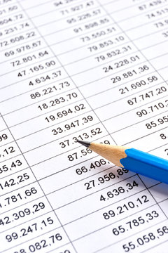 Blue pencil on a sheet of white paper with printed financial numerical data table with columns. Concept for accounting, budget, profit, tax and financial review. Vertical image with selective focus 