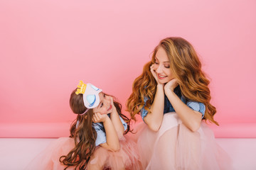 Beautiful young woman with trendy hairstyle sitting on the floor next to charming little girl and...