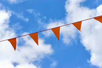 A row of orange triangle pennant banner flags on Koningsdag. A national holiday in the Netherlands against a blue sky with clouds and copy space
