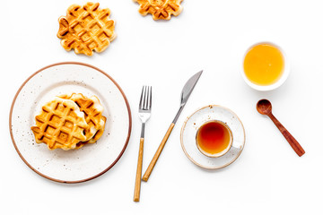 Breakfast with Belgian waffles with honey, tea, knife, fork and spoon on white background top view