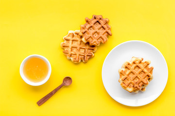 Breakfast with Belgian waffles with honey and spoon on yelllow background top view