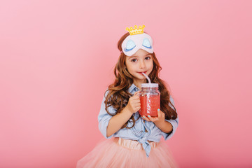 Amazing cute little girl with princess mask on head, long brunette hair drinking juice from glass...