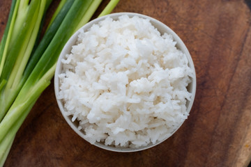 Streamed rice is asian appetizer in white bowl puton wood background  with green onions.Top view photo.