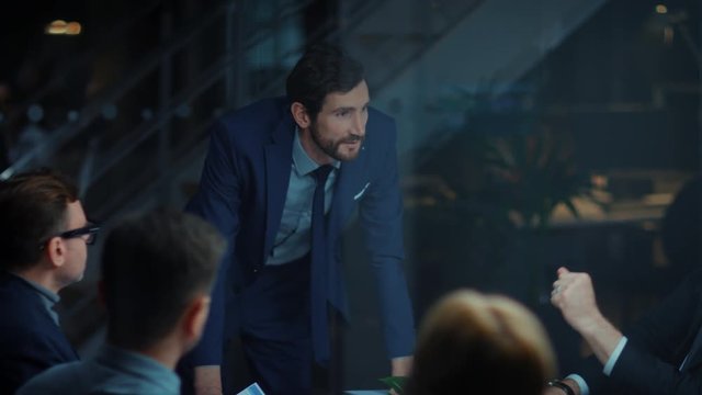 Corporate Meeting Room: Confident and Handsom Executive Director Decisively Leans on a Conference Table and Delivers Report to a Board of Executives about Company&rsquo;s Record Breaking Revenue