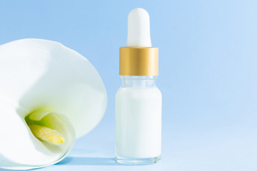 Natural cosmetics: serum with dropper and Calla Lily flower on blue background.