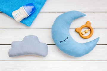 Put baby into bed with moon pillow, clouds, feeding bottle and toy on wooden background top view