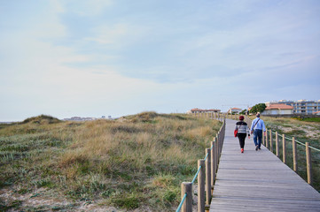 couple walking on the Wooden footwalk over the dunes in portugal near the beach
