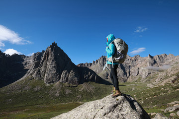 Woman hiker with backpack hiking on high altitude mountain top