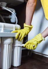 Plumber in yellow household gloves changes water filters. Repairman changing water filter...