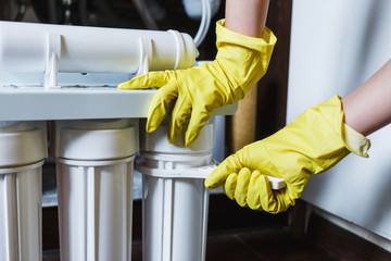 Close up Plumber in yellow household gloves changes water filters. Repairman changing water filter...