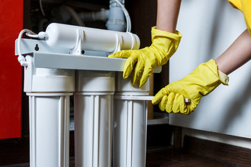 Plumber in yellow household gloves changes water filters. Repairman changing water filter cartridges in kitchen. Drinkable water filtration system in the kitchen. Clean water at home