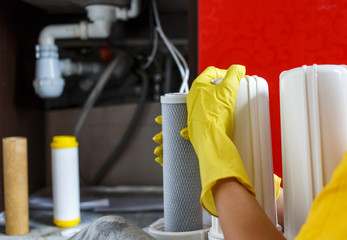 Close up Plumber in yellow household gloves changes water filters. Repairman changing water filter...