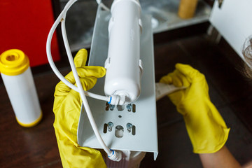 Plumber in yellow household gloves changes water filters. Repairman changing water filter...