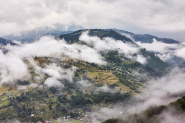 Summer mountain panorama. Small wooden house cottage and barn on green mountain valley on bright foggy sky, clouds and mountain