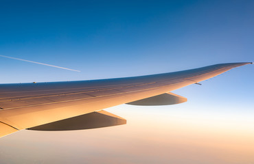 Wing of plane over the city. Airplane flying on blue sky. Scenic view from airplane window. Commercial airline flight in the morning with sunlight. Plane wing above clouds. Flight mechanics concept.