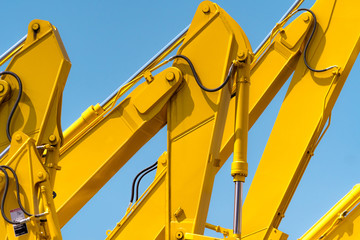 Yellow backhoe with hydraulic piston arm against clear blue sky. Heavy machine for excavation in...
