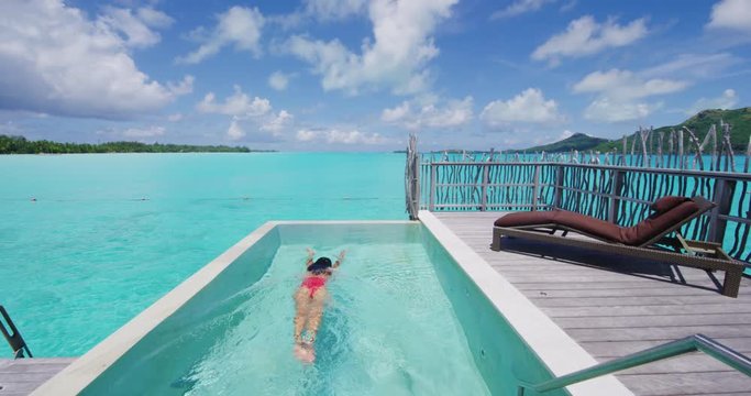 Luxury summer vacation - Woman swimming underwater in bikini in infinity pool at travel hotel resort at ocean beach lagoon. Elegant lady relaxing swimming enjoying holidays at pool. RED SLOW MOTION.
