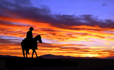 Fototapeta na wymiar Cowboy on horseback rides into the sunset