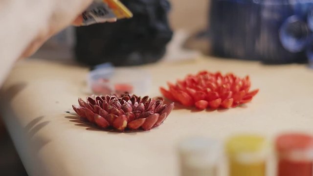 Female artist is making a design of decorative flowers with bright painted nut shells