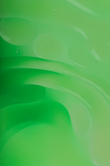 Blurred abstract background. Macro shot of oily liquid. Green circles and wavy lines of different sizes. Blur, vertical, a lot of free space for text, nobody, macro. Concept of design.