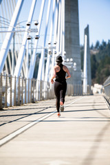 Girl in black tight sportswear trains run for weight loss on Tilikum Crossing Bridge