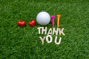 Golf ball with thank you word and tees are on green grass.