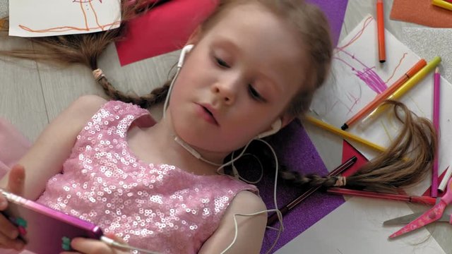 little girl lying on the floor uses the phone, listens to music